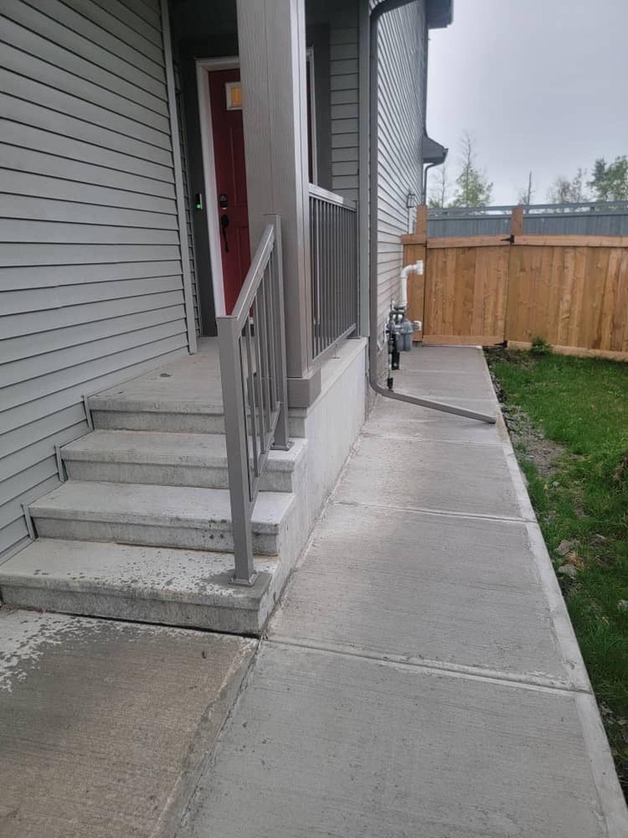 A residential house with a concrete front porch, a wooden fence, and a red door.