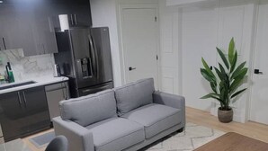 Una cocina moderna con armarios oscuros, un refrigerador y una encimera. En la zona de estar, hay un sofá gris y una mesa de centro de madera.