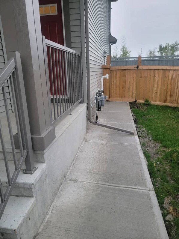 A concrete pathway leading to a house with a metal railing and a wooden fence in the background. - Shiloh and Still Serene 2bed Basement (Edmonton)