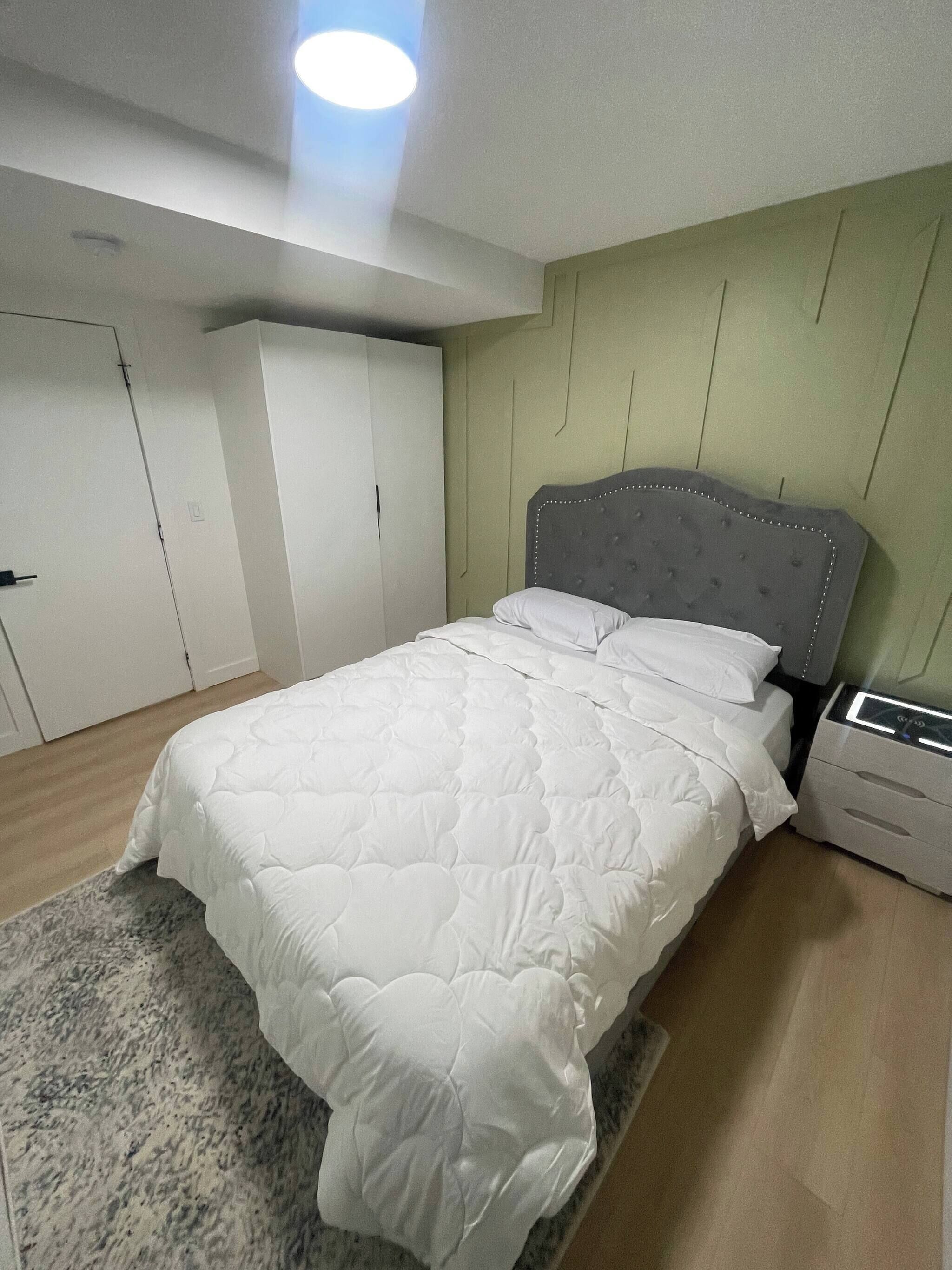 A bedroom with a bed, a nightstand, a wardrobe, and a ceiling light.