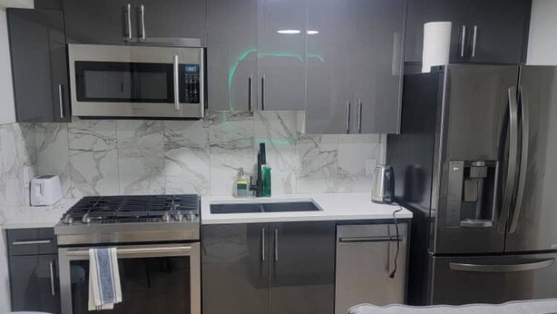 Una cocina moderna con electrodomésticos de acero inoxidable, salpicadero de mármol y armarios grises.