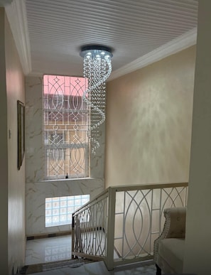 Una escalera con barandilla blanca, un candelabro y una ventana con celosías metálicas decorativas.