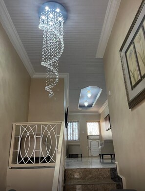 A staircase with a decorative chandelier, a framed picture on the wall, and a ceiling light fixture.