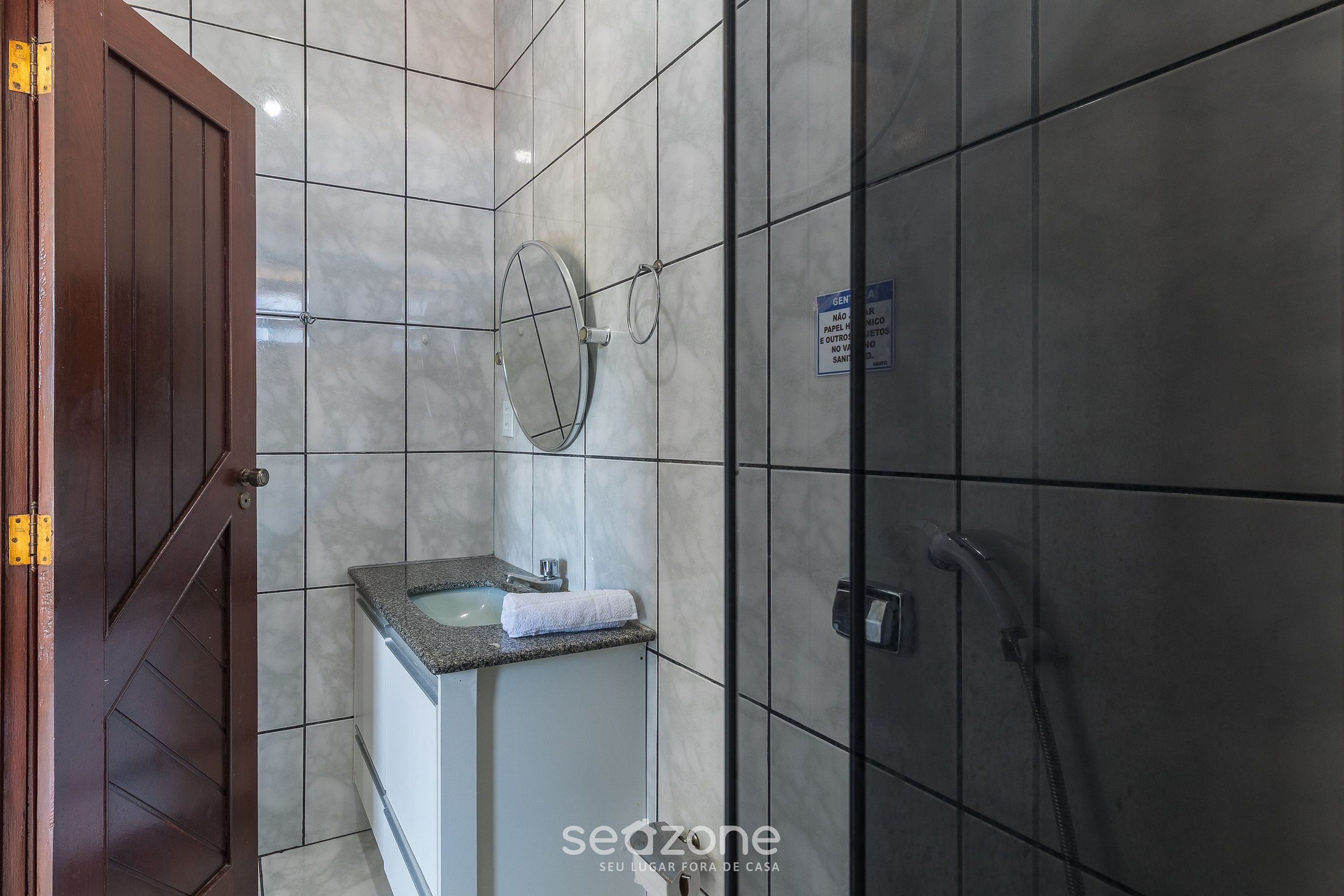 A bathroom with a wooden door, a sink with a mirror, and a shower area.