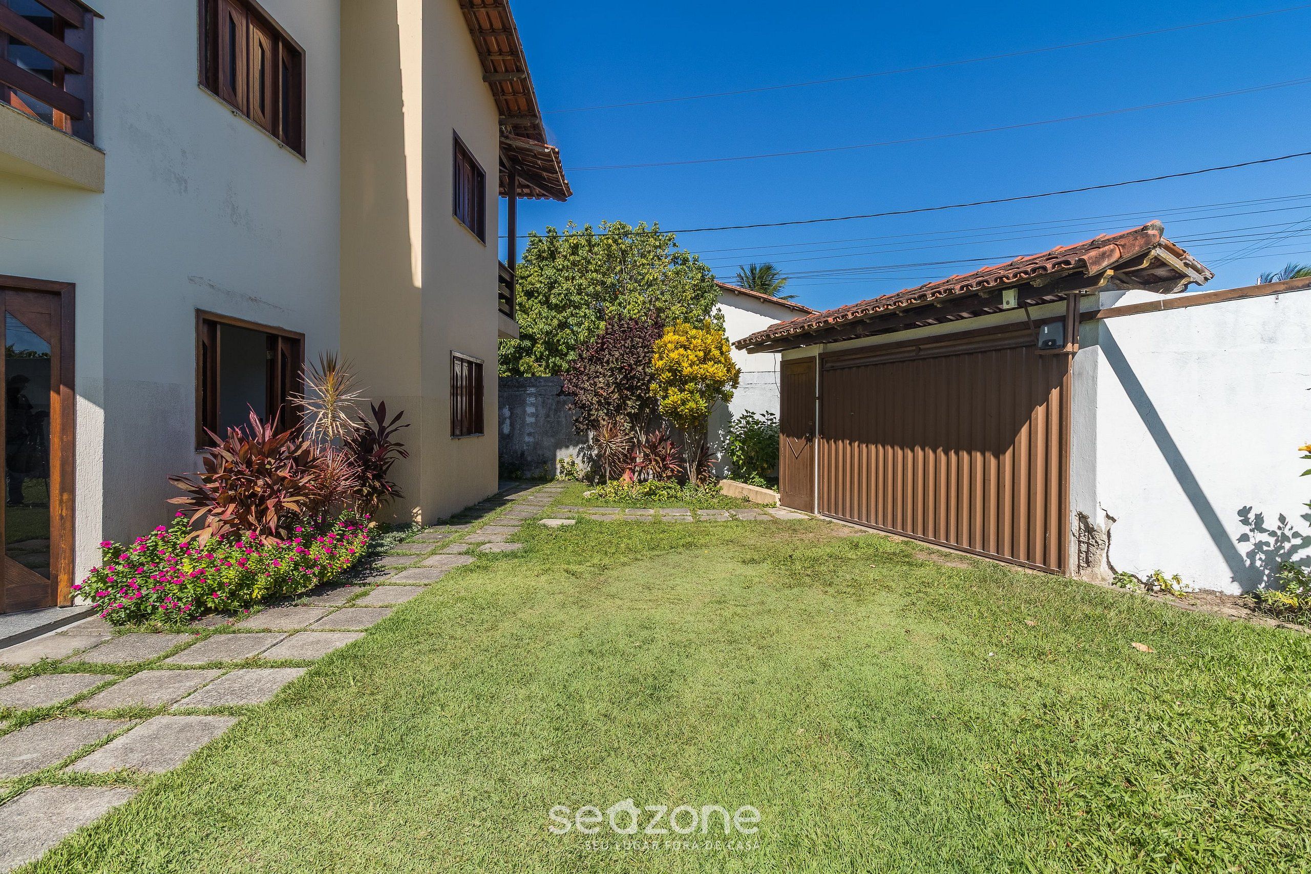 A residential property with a well-maintained lawn, a wooden fence, and a white building with a brown roof.