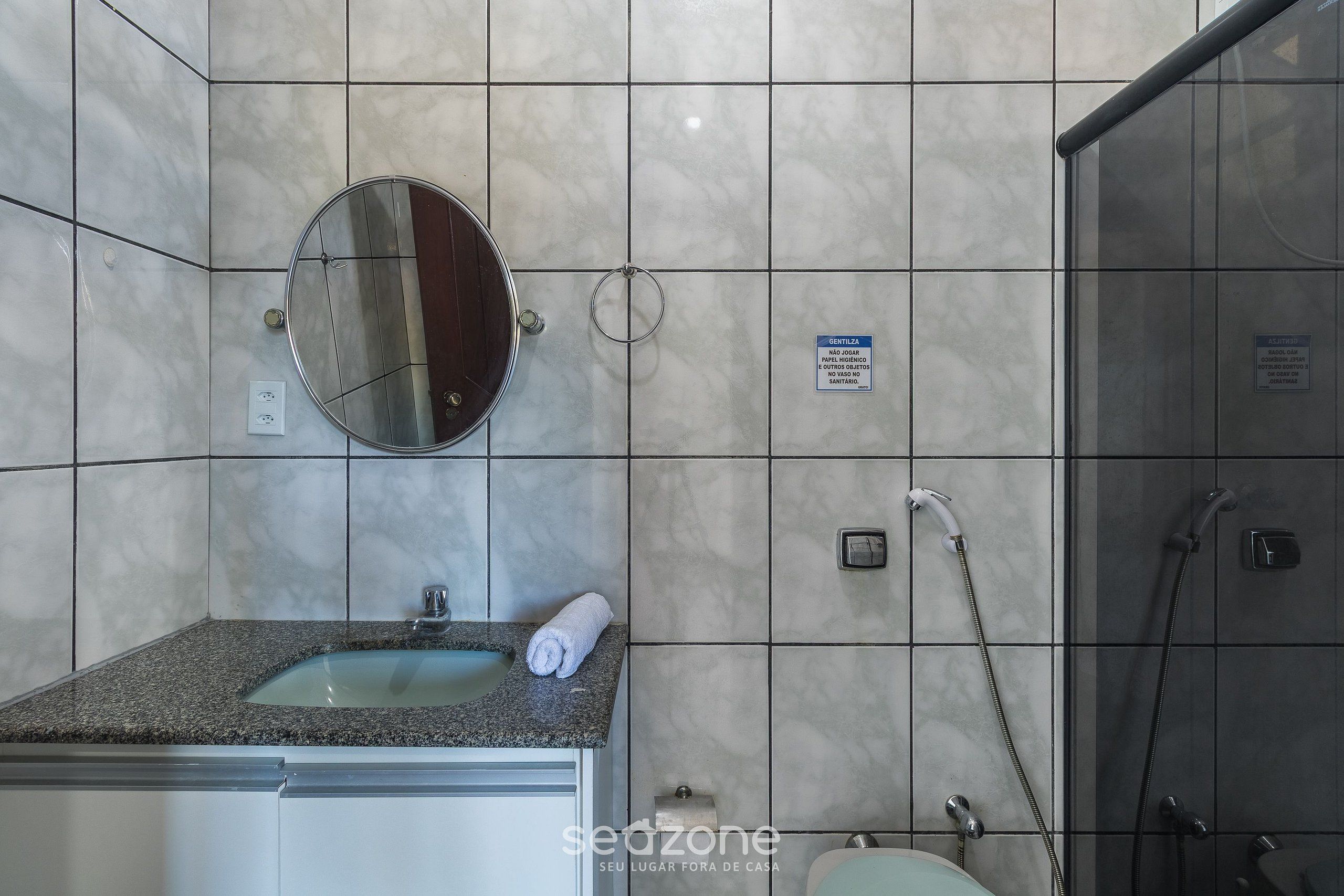 A bathroom with a granite countertop sink, a round mirror, a towel, a shower with a handheld showerhead, and a sign indicating a private bathroom.