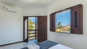 Una camera d'albergo con un letto, una finestra con persiane in legno, un condizionatore d'aria e vista all'esterno.