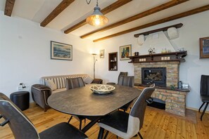 Ein gemütliches Wohnzimmer mit einem runden Tisch, bequemen Sitzgelegenheiten, einem Kamin und Holzbalken an der Decke.