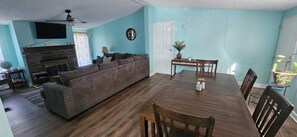 A living room with a sofa, a dining table, chairs, a fireplace, and a TV mounted on the wall. - Affordable family beach getaway - just a 5-minute walk to the sand! (Panama City Beach)