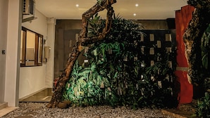 Un giardino interno moderno con un grande albero, un vialetto di ciottoli e una struttura muraria rossa.