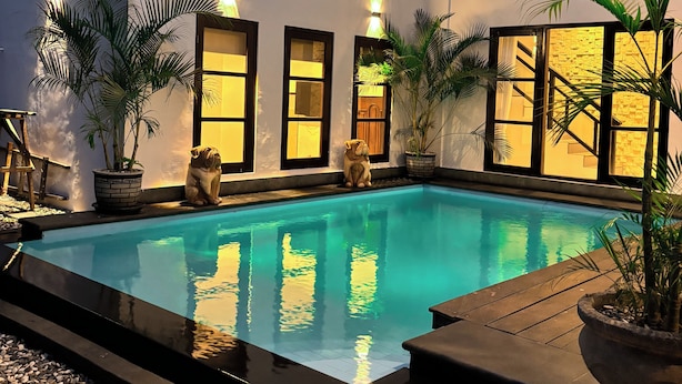 Una piscina con bordo in pietra, circondata da piante in vaso e un edificio bianco con numerose finestre.