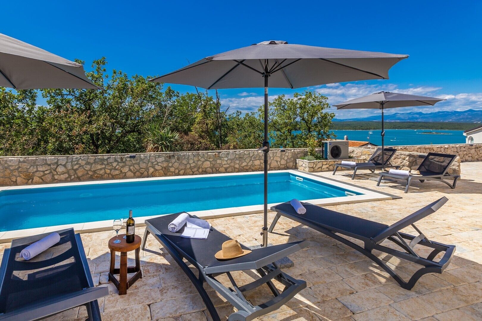 Área de piscina com espreguiçadeiras, guarda-sóis e vista para o mar.