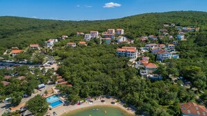 Vue aérienne d’un quartier résidentiel situé sur une colline, avec des maisons, une piscine et une plage.