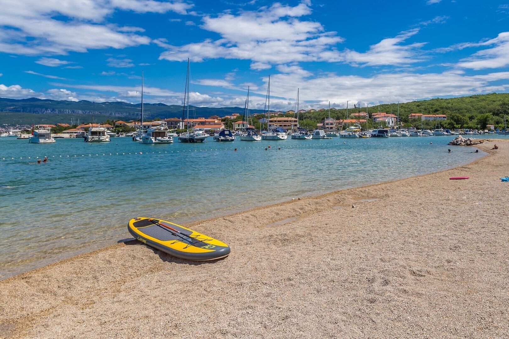A beach with a yellow kayak, boats, and houses in the background.