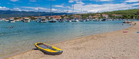 A beach with a yellow kayak, boats, and houses in the background.