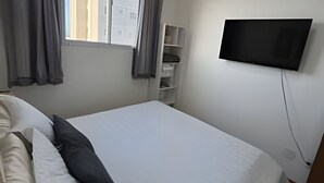 Una camera d'albergo con un letto, una TV fissata al muro, una finestra con tende e un piccolo mobiletto.
