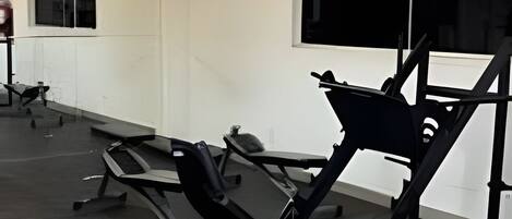 Un gimnasio con equipo de ejercicio, una ventana y un aparato de aire acondicionado.