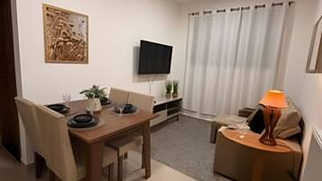 Ein modernes Wohnzimmer mit Esstisch, Stühlen, Fernseher, Lampe und einem Bild an der Wand.