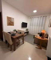 Una sala de estar moderna con una mesa de comedor, sillas, un televisor, una lámpara y un cuadro en la pared.