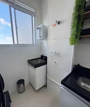 Una cocina pequeña con ventana, un lavabo, un cubo de basura y un mueble pequeño.