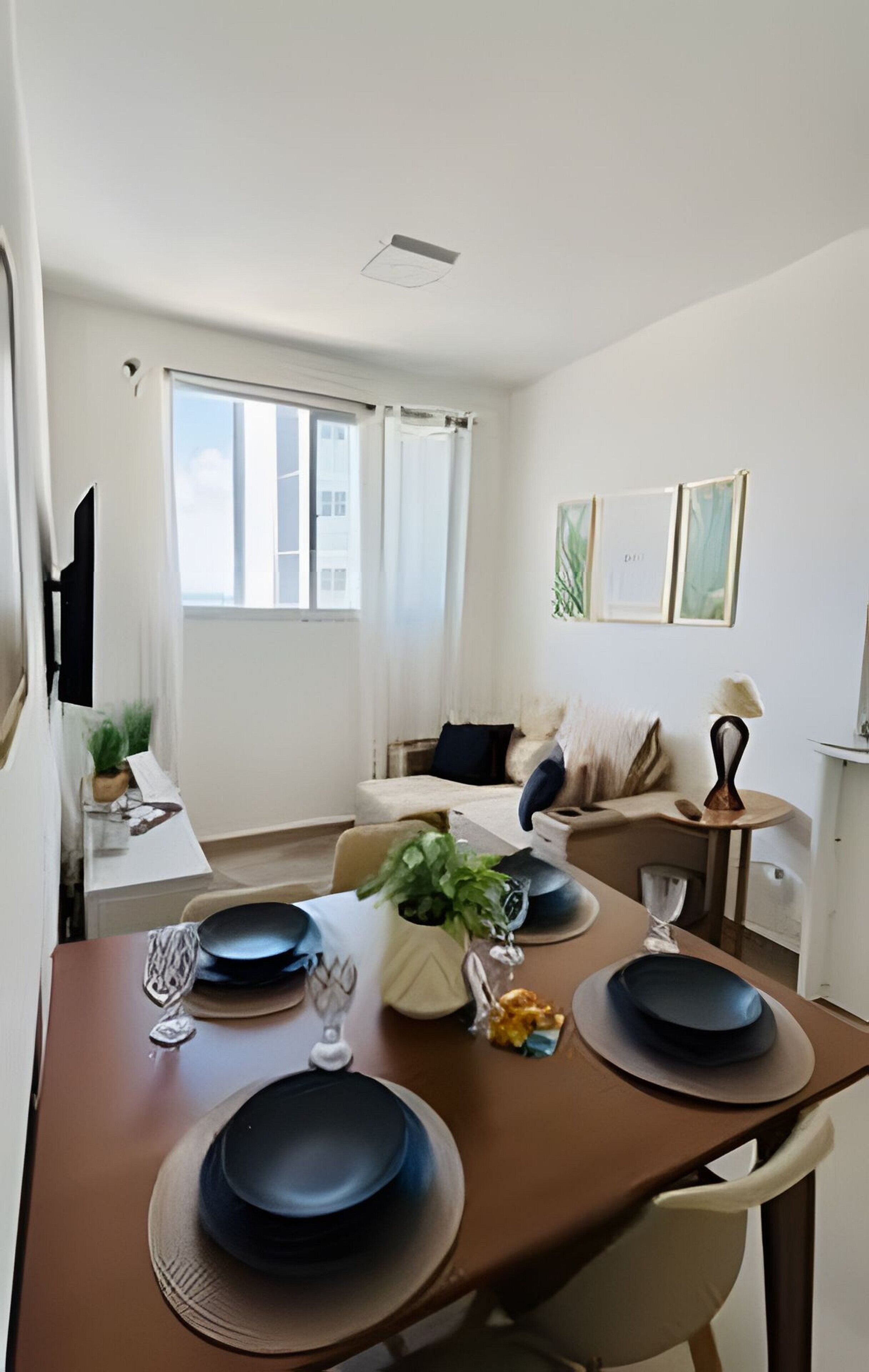 Uma área de refeições com uma mesa posta para quatro pessoas, um sofá, uma pequena mesa lateral com abajur e uma janela com cortinas.