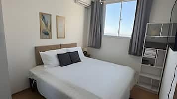 Ein Hotelzimmer mit Bett, Schreibtisch, Stuhl, einem Fenster mit Vorhängen und Wandbildern.