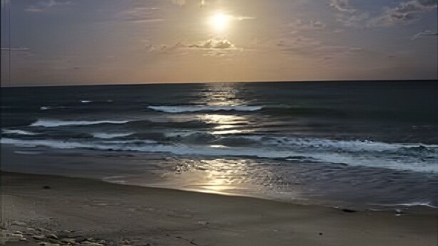 Una spiaggia con onde, cielo sereno e il sole che tramonta o sorge.