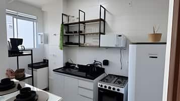 Eine kleine Küche mit weißen Schränken, einem Gasherd, einem Backofen und einem Kühlschrank.