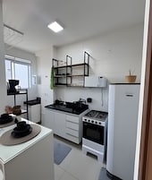 Una cocina compacta con armarios blancos, estufa a gas, horno empotrado y refrigerador.