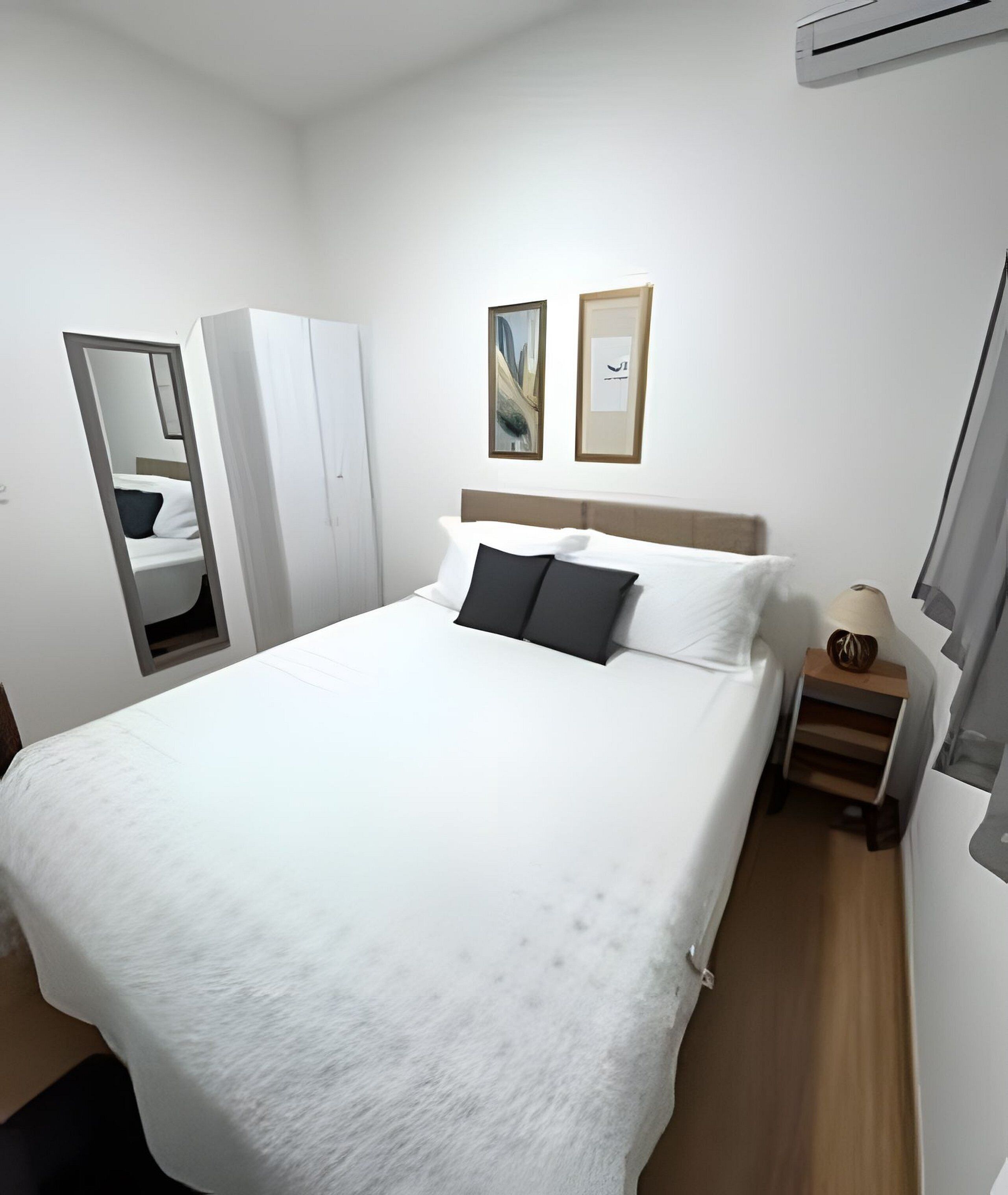 A hotel room with a bed, a nightstand, a mirror, and two framed pictures on the wall.