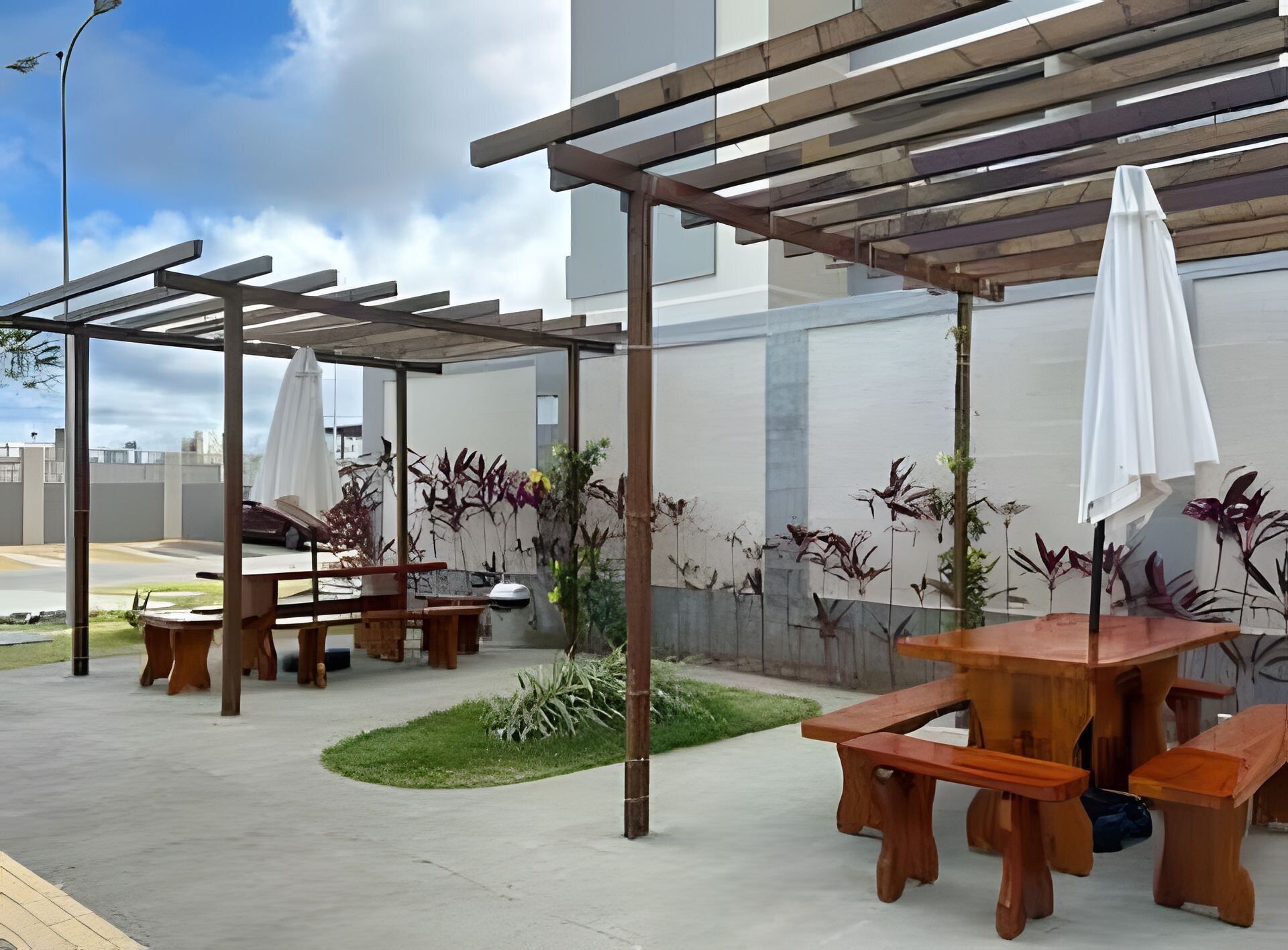An outdoor patio area with wooden tables and benches, covered by pergolas, and surrounded by potted plants.