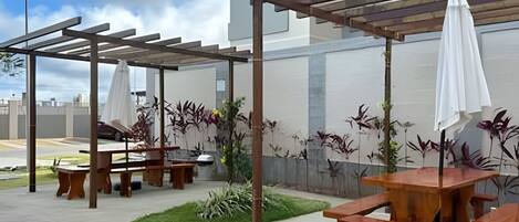 An outdoor patio area with wooden tables and benches, covered by pergolas, and surrounded by potted plants.