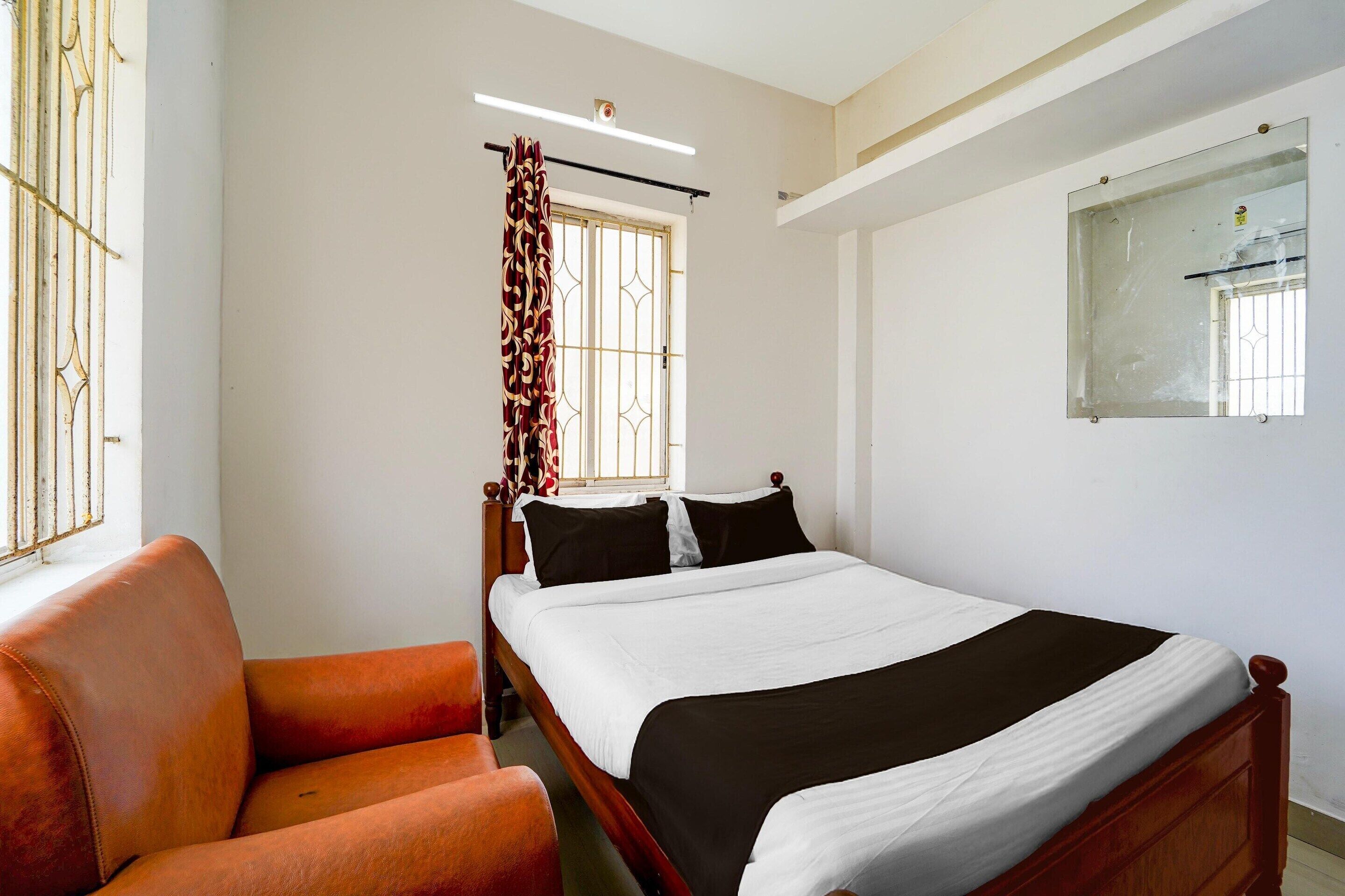 A bedroom with a bed, a chair, a window with bars, and a mirror on the wall.