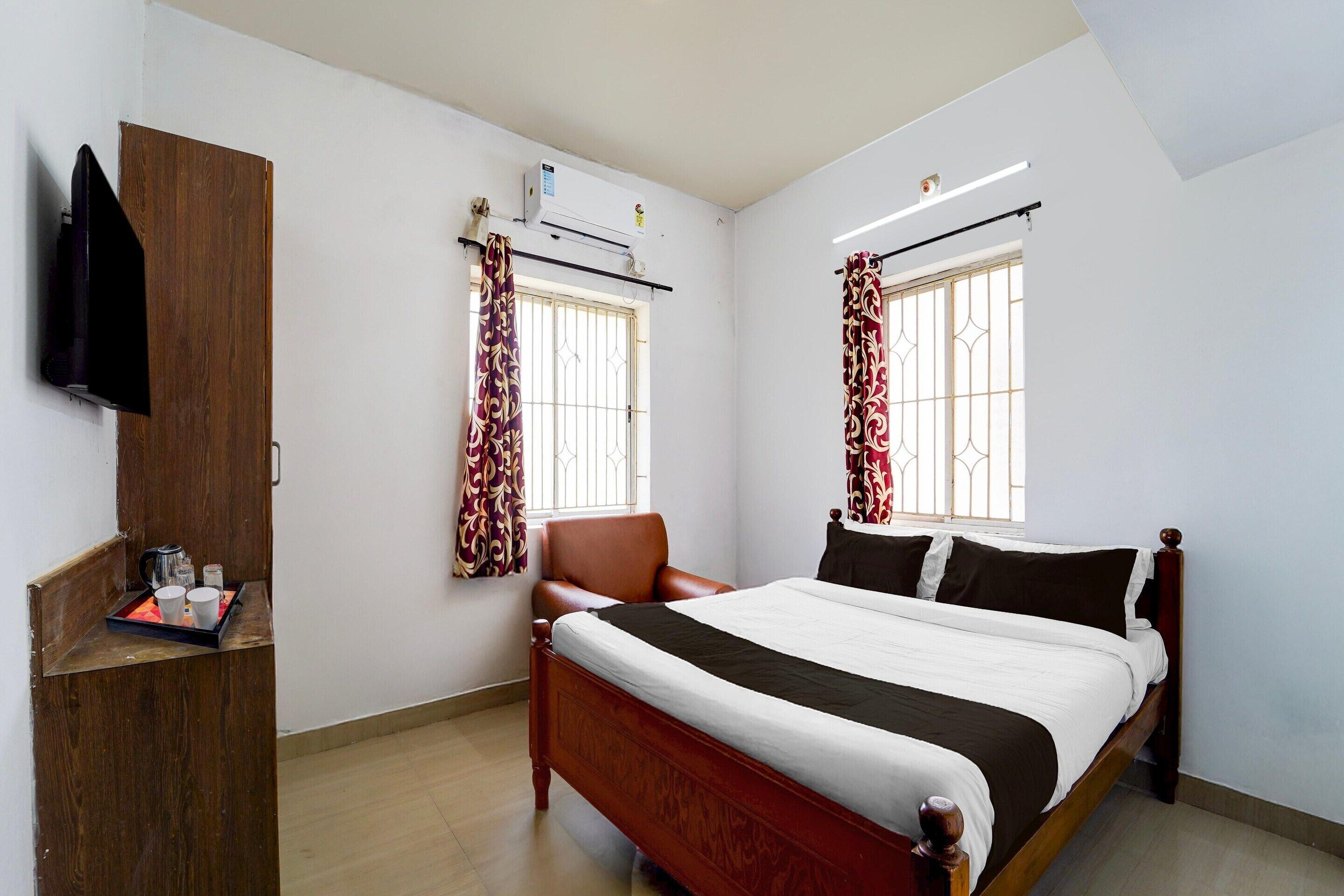 A bedroom with a bed, a wooden wardrobe, a chair, a window with curtains, and an air conditioning unit.