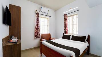 A bedroom with a bed, a wooden wardrobe, a chair, a window with curtains, and an air conditioning unit.