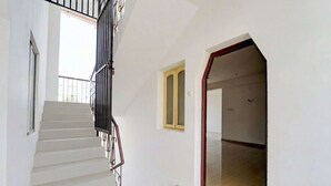 Eine Treppe mit weißen Stufen und schwarzen Geländern, ein kleines Fenster und eine Tür zu einem Innenraum.