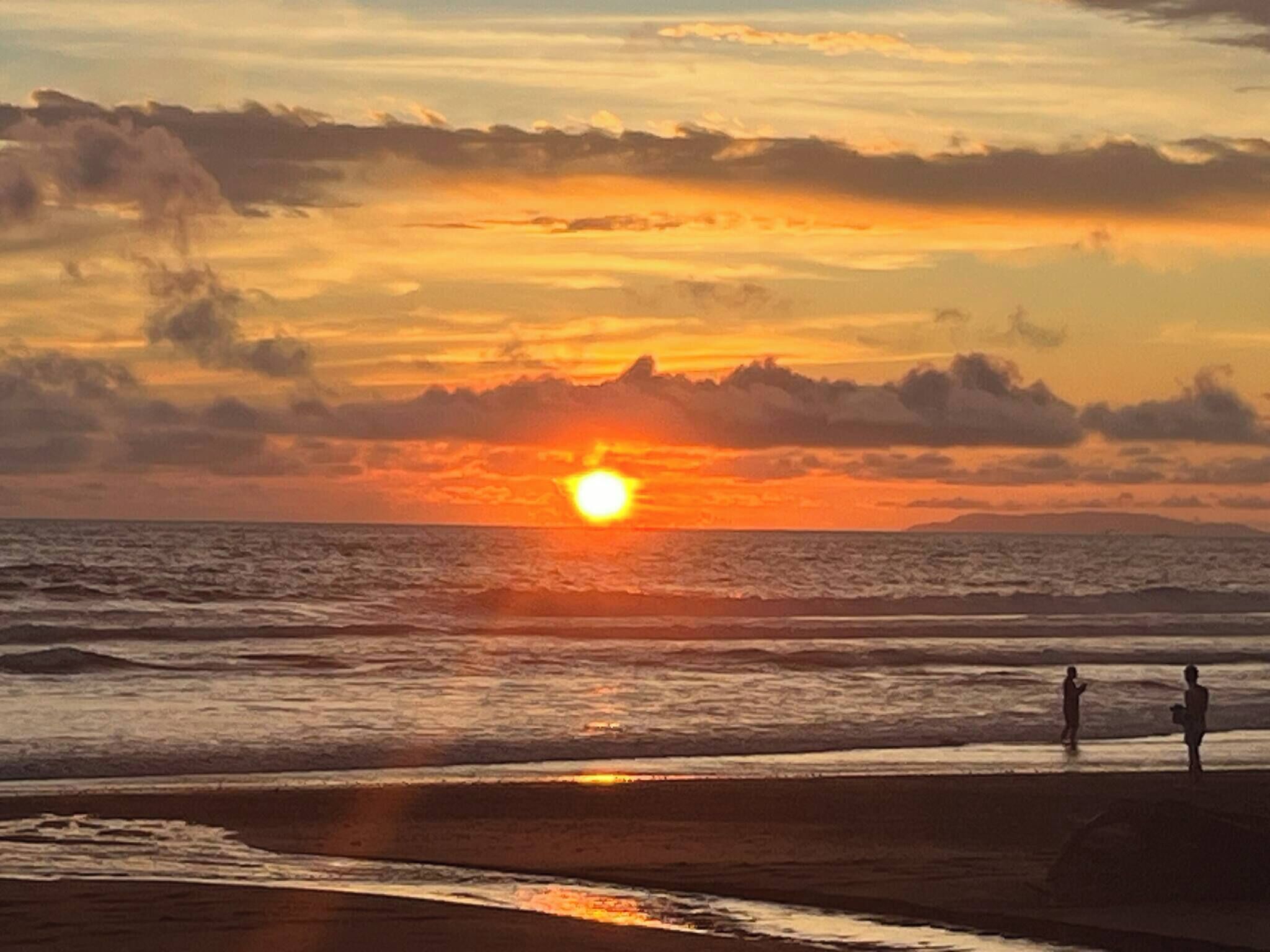 Una puesta de sol sobre el océano con dos personas en la playa.