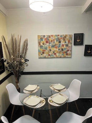 A dining area with a glass table, white chairs, and a wall-mounted abstract painting. - Villa a Block Away to the Beach (Jacó)