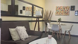 A modern living area with a dark brown sofa, a white coffee table, and a dining table with chairs. There are framed artworks on the walls and a ceiling fan above. - Villa a Block Away to the Beach (Jacó)