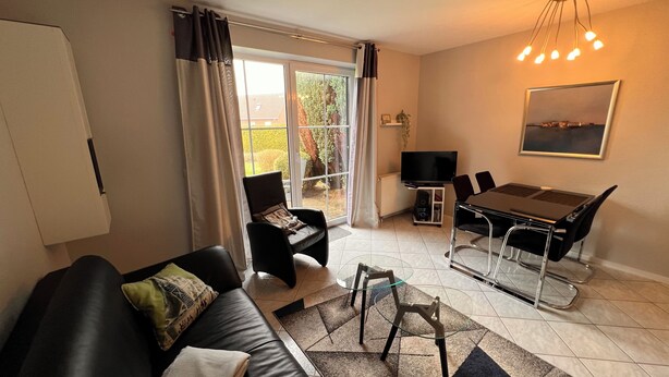 Een moderne woonkamer met een bank, een glazen salontafel, een eettafel met stoelen, een televisie en een groot raam met gordijnen.