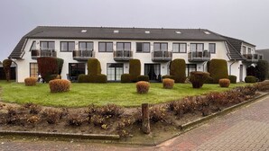 Een woonhuis met twee verdiepingen, een plat dak, meerdere balkons en een verzorgd gazon met diverse heesters.