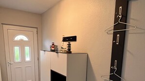 Een gang met een witte deur, een zwart-wit koelkast, een zwart-witradiator en een zwart-wit kapstok.