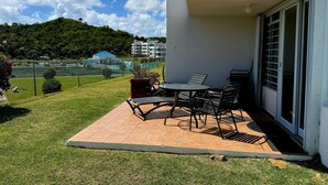 Un patio con una mesa y sillas, una planta en maceta y vistas a una colina con edificios al fondo.