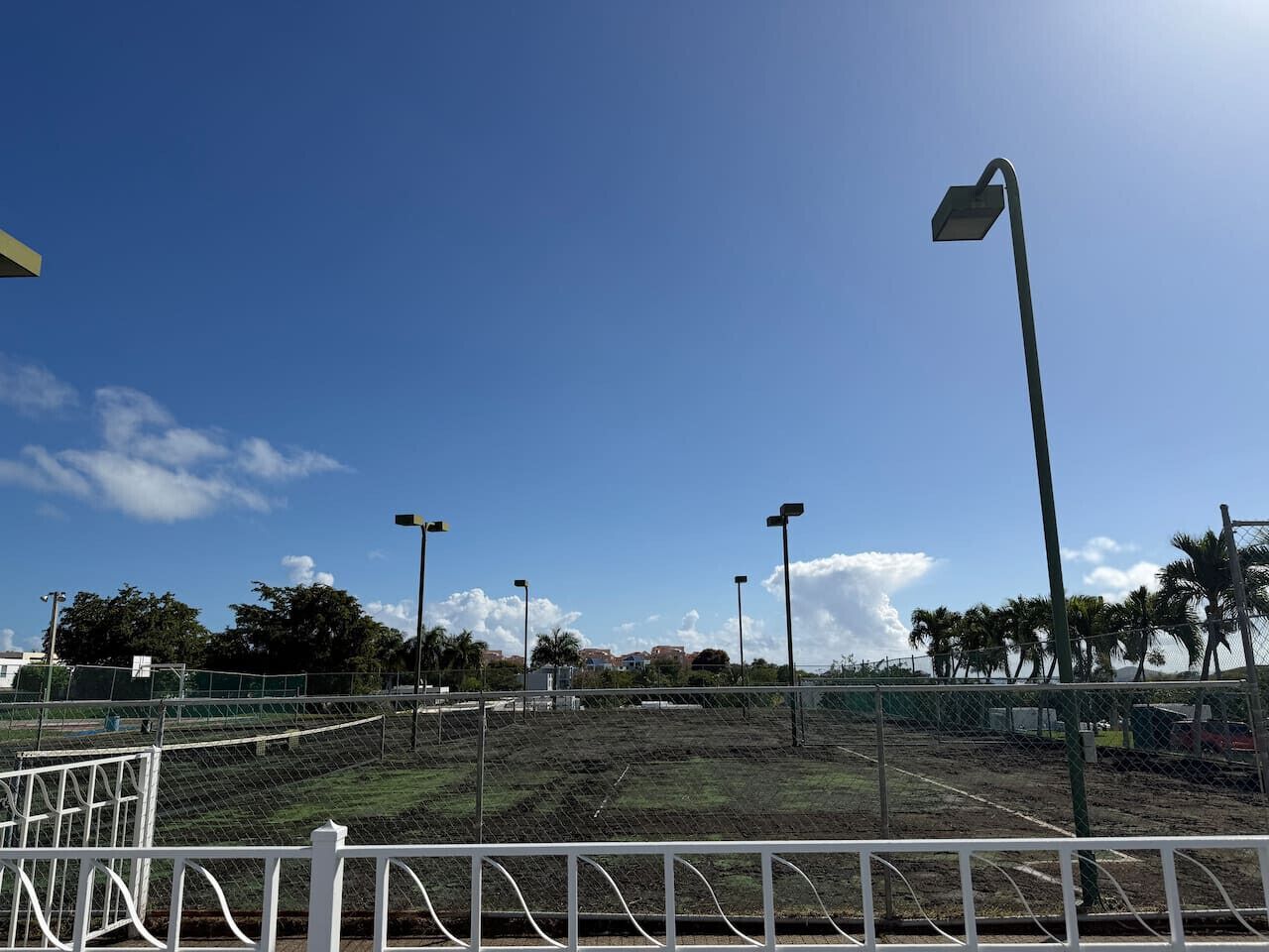 Un campo deportivo cercado con varias columnas de luz y un cielo azul despejado.