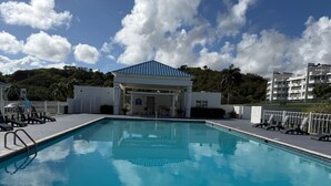 Piscina con sillas de descanso, un área techada y un edificio al fondo.