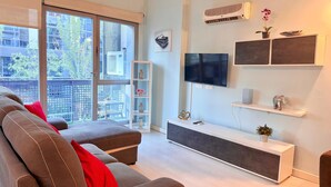 A modern living room with a grey sofa, a TV, and a white console table. - Oshun Estudio Deluxe D312 (Madrid)