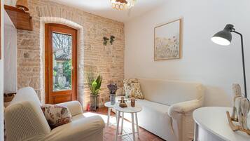 A cozy living room with a stone wall, a wooden door, a white sofa, a small round table, and a hanging light fixture.