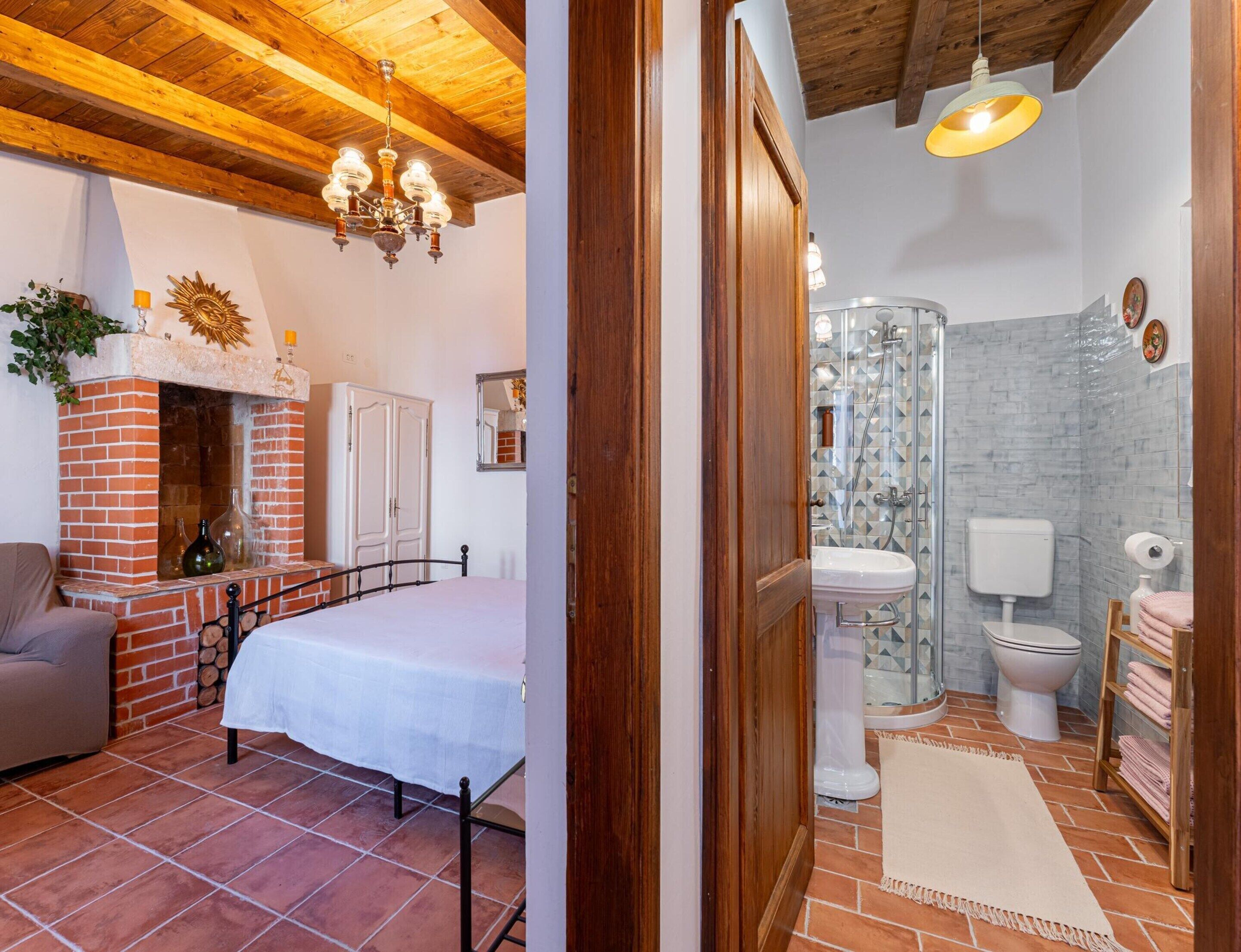 A bedroom with a bed, a fireplace, and a wooden ceiling.