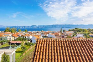 Eine Küstenstadt mit terrakottafarbenen Dächern, blauem Himmel und Blick auf das Meer und ferne Berge.