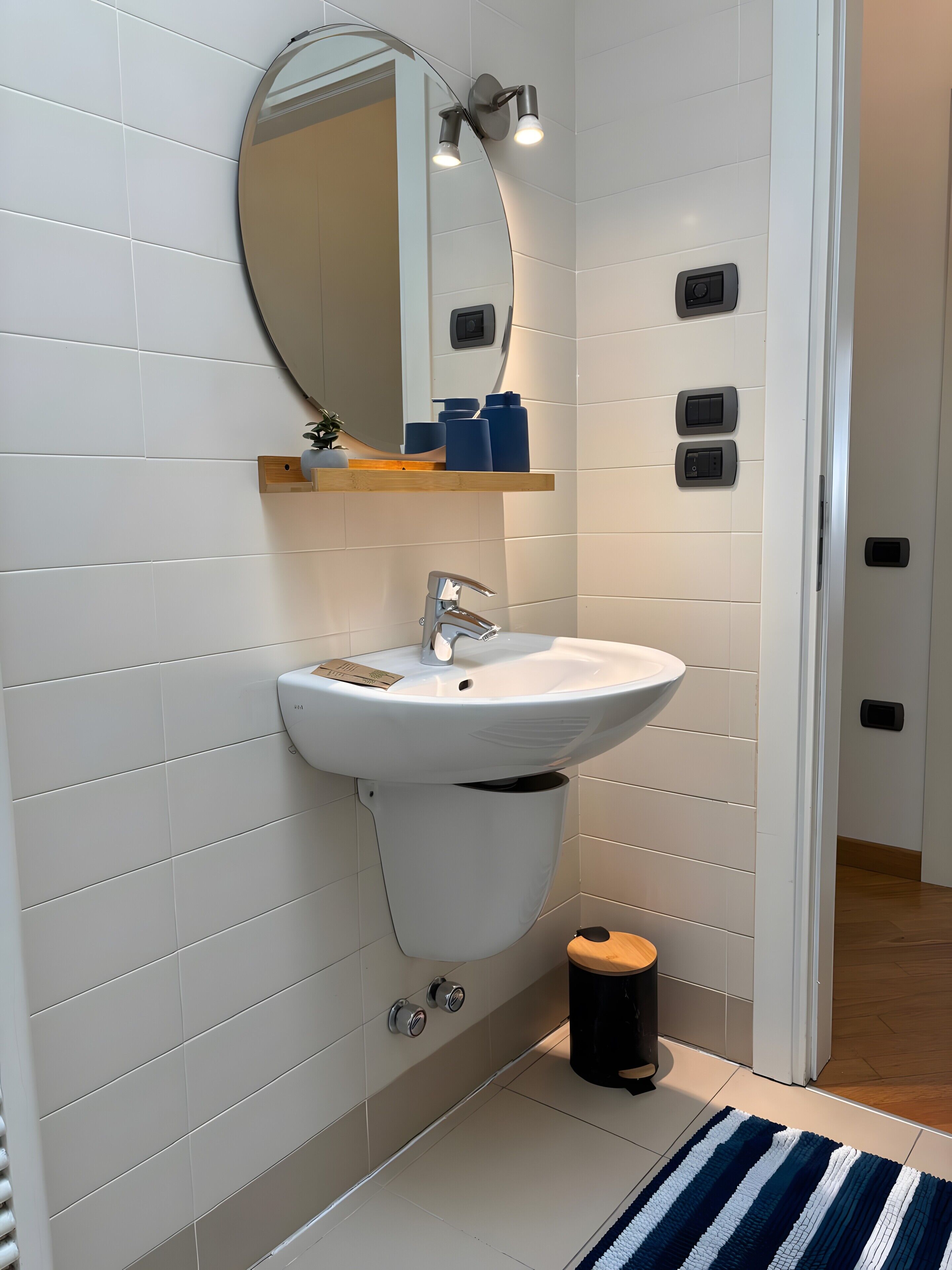 A bathroom with a white sink, a mirror, and a small trash bin.